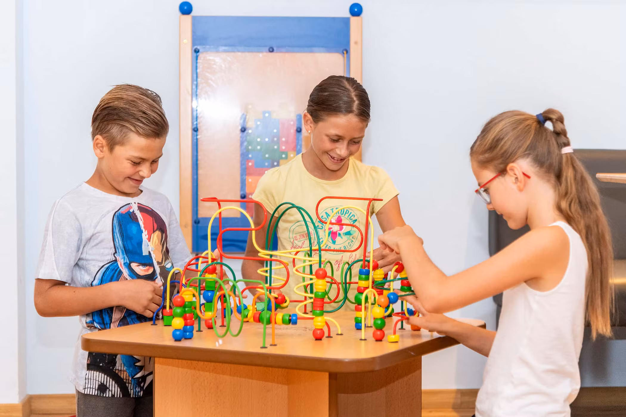 Drei lächelnde Kinder spielen mit einem bunten Perlenlabyrinth im Spielzimmer des Agriturismo Brunnerhof.