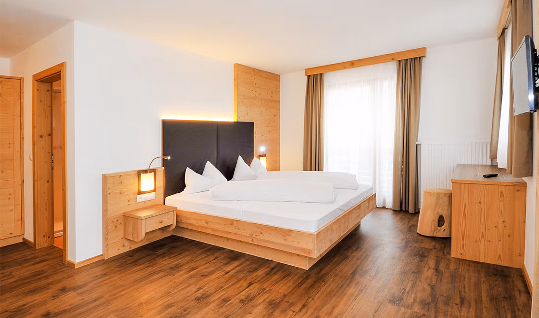 Gemütliches Doppelzimmer des Brunnerhofs mit Naturbett, Nachttisch, TV und Parkettboden.