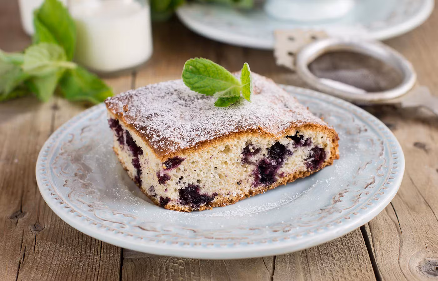 Hausgemachtes Blaubeerkuchenstück mit Puderzucker und Minze, Symbol der authentischen Küche des Agriturismo.