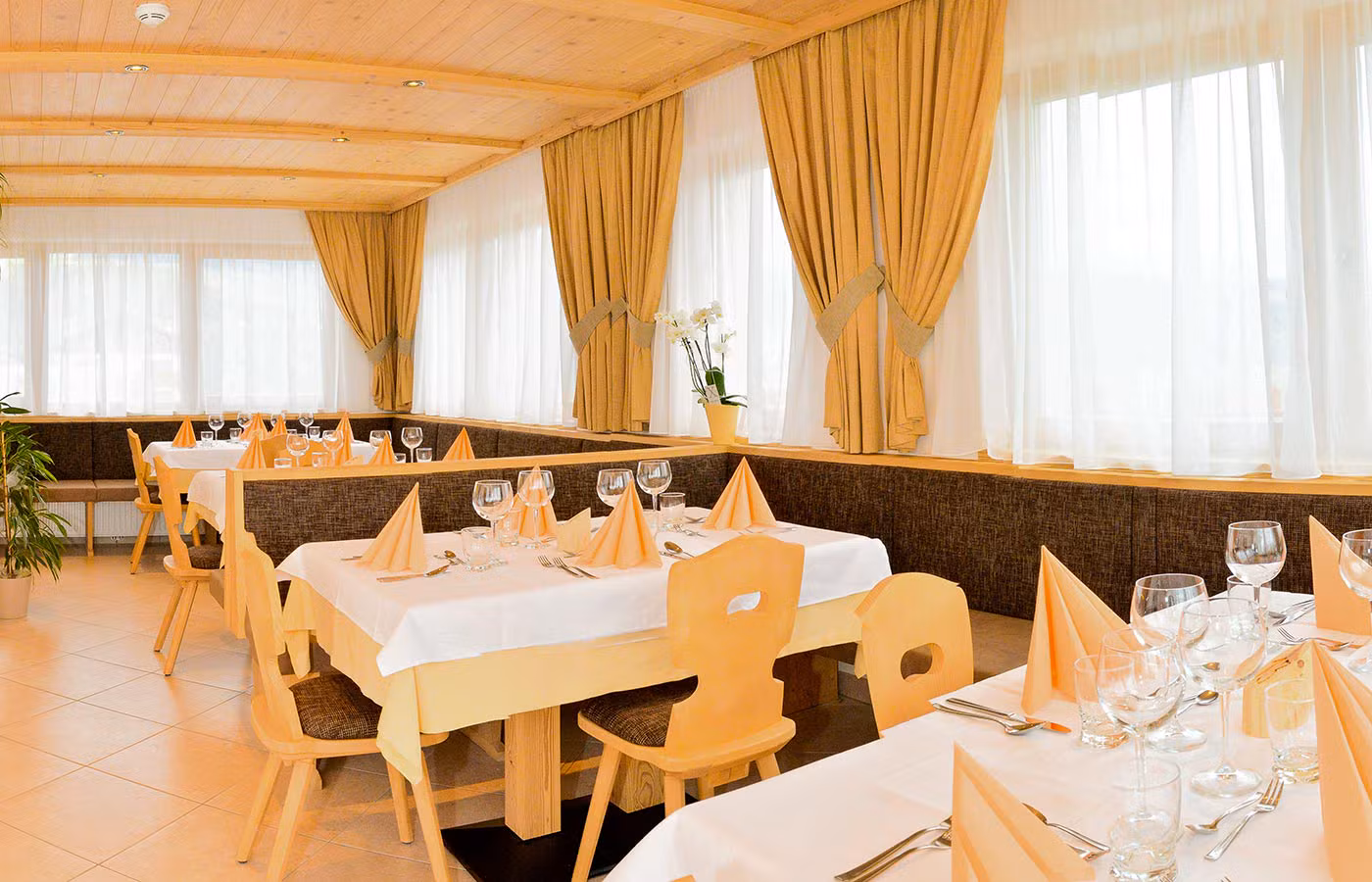 Großer Speisesaal des Agriturismo Brunnerhof mit gedeckten Tischen und Fenstern mit goldenen Vorhängen.