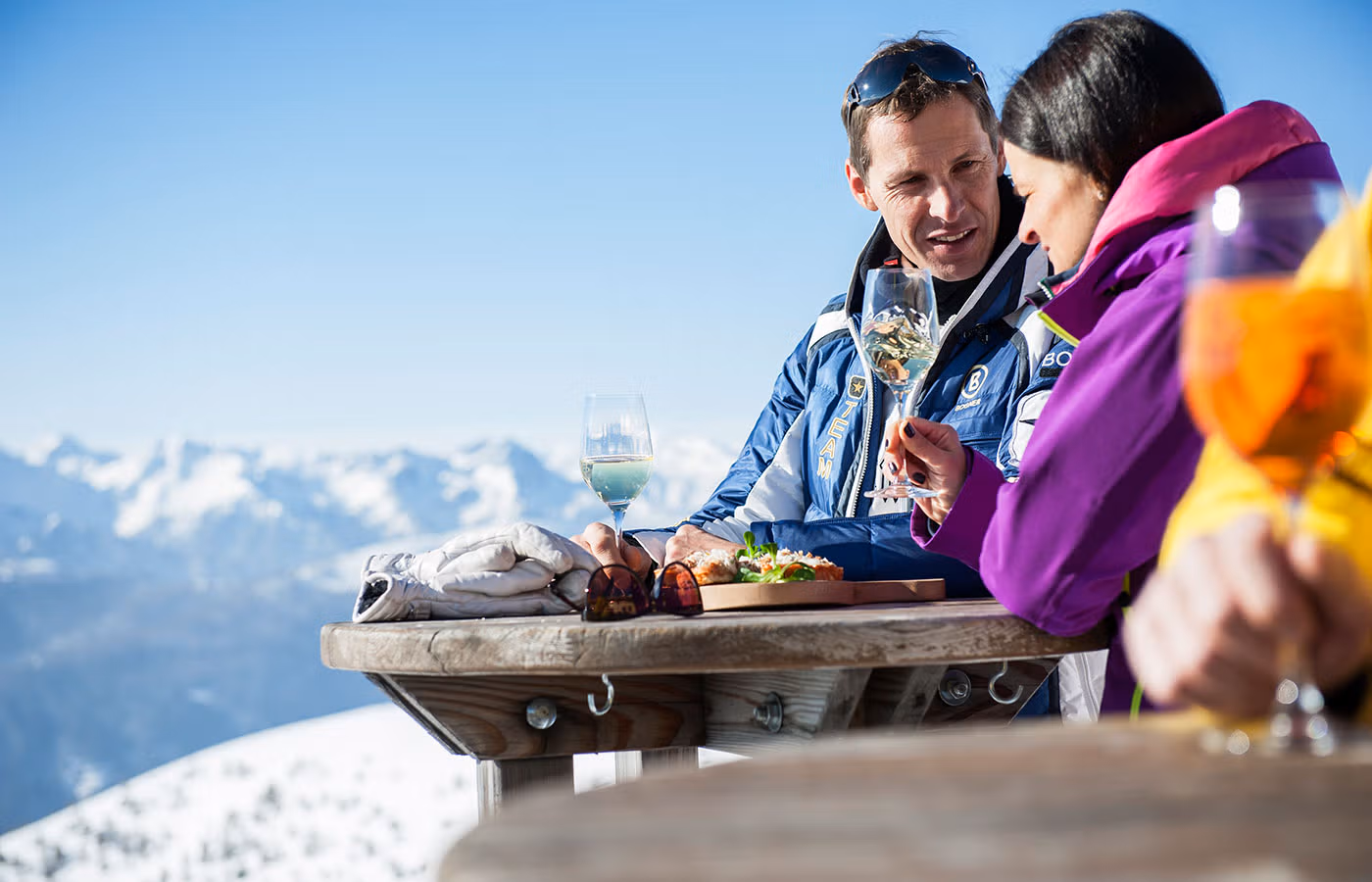 Coppia sorridente gusta un aperitivo con vista sulle Dolomiti innevate, un momento di relax in Val Pusteria.