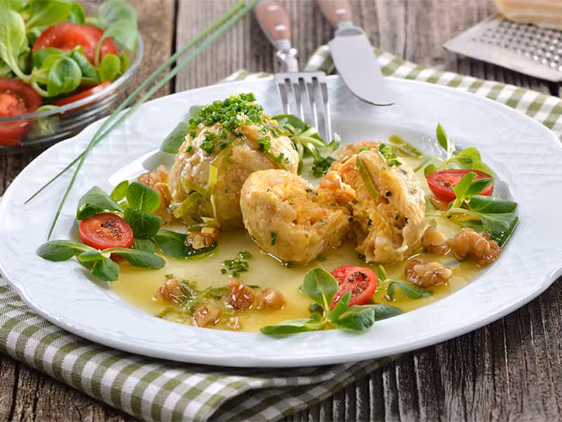 Traditionelle Südtiroler Canederli mit frischem Salat, Walnüssen und Sauce, eine authentische Delikatesse unseres Agriturismo.