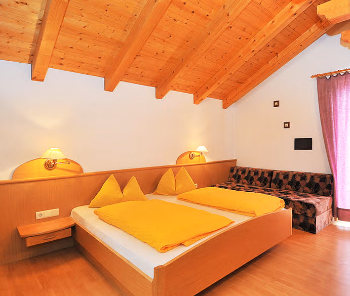 Camera matrimoniale "Eichenkrone" del Brunnerhof con letto in legno naturale, soffitto a travi e divano.