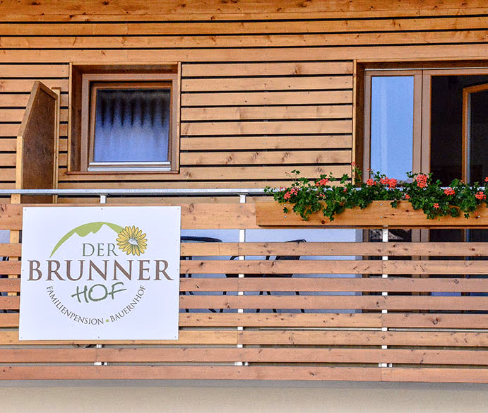 Balcone in legno con fioriera e insegna "Der Brunnerhof", agriturismo in Val Pusteria.