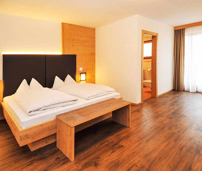 Ampia camera matrimoniale in agriturismo con letto in legno naturale, piumoni bianchi, illuminazione soffusa e pavimento in parquet.