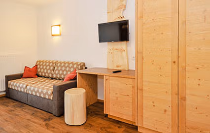 Accogliente camera in agriturismo con divano letto, TV e mobili in legno naturale, ideale per vacanze in famiglia in Val Pusteria.