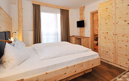 Camera matrimoniale Zirmspitz con arredi in legno naturale, letto comodo e armadio spazioso, ideale per vacanze in famiglia in Val Pusteria.