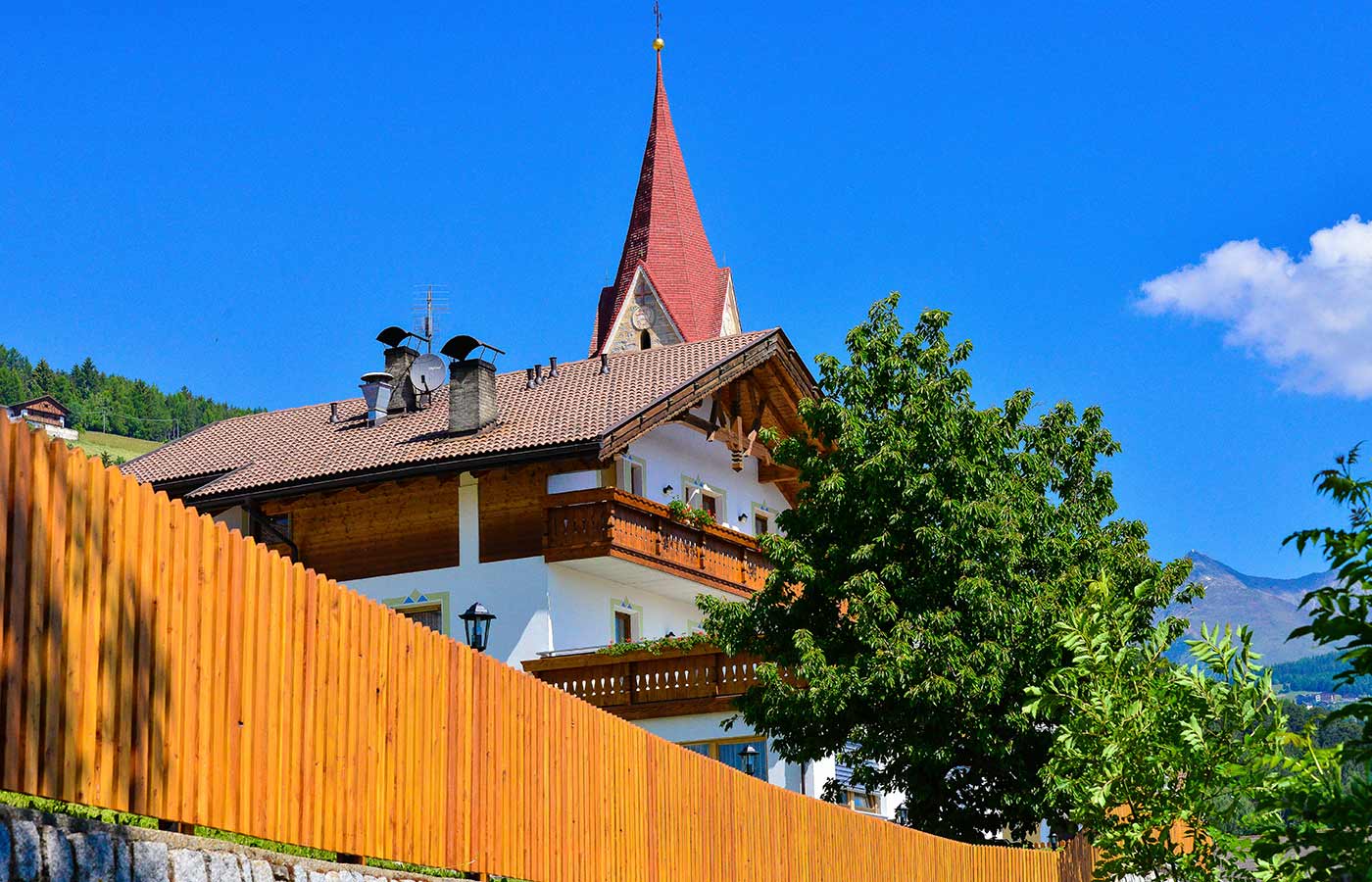 Detailaufnahme eines Daches und ein Kirchturm ragt im Hintergrund in die Höhe