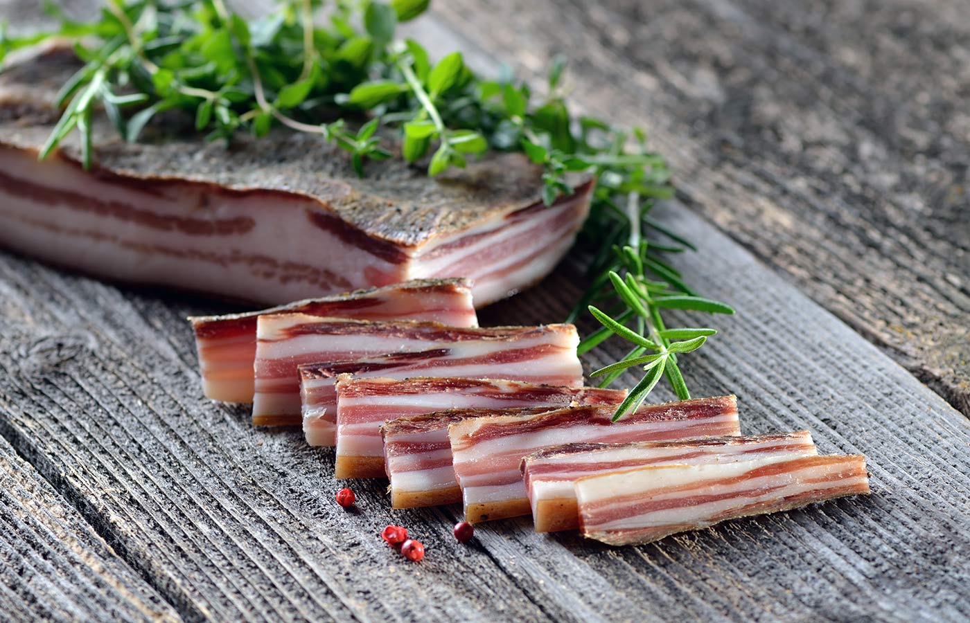 Pancetta tagliata a fettine con erbe naturali su un tavolo in legno